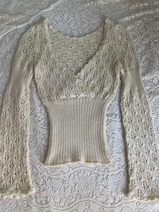 A cream-colored, long-sleeve knit top with a lace overlay and ribbed bodice, laid flat on a white lace background.
