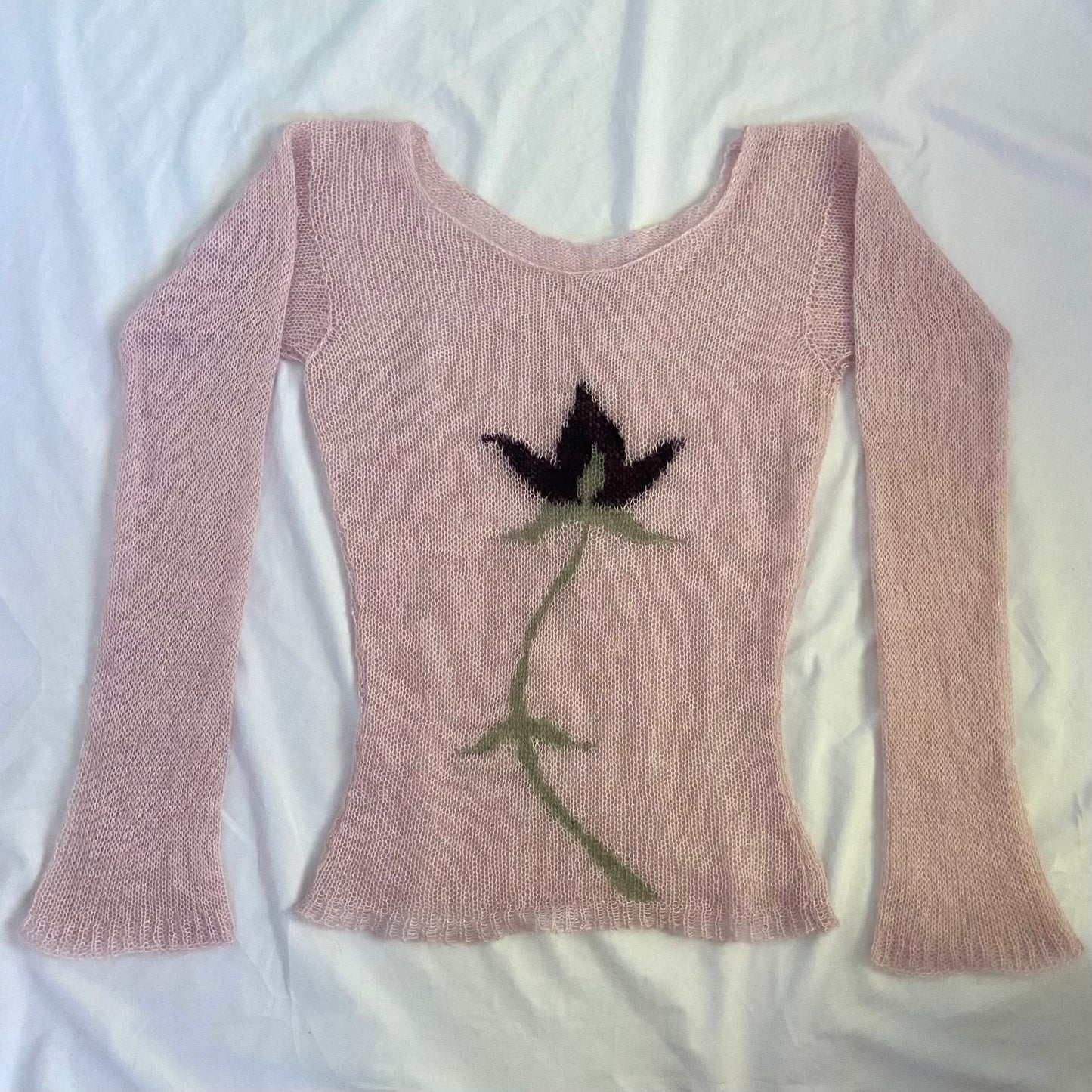 Image is of a sheer light pink mohair long sleeve top with an intarsia flower on the front. The flower is black and green.