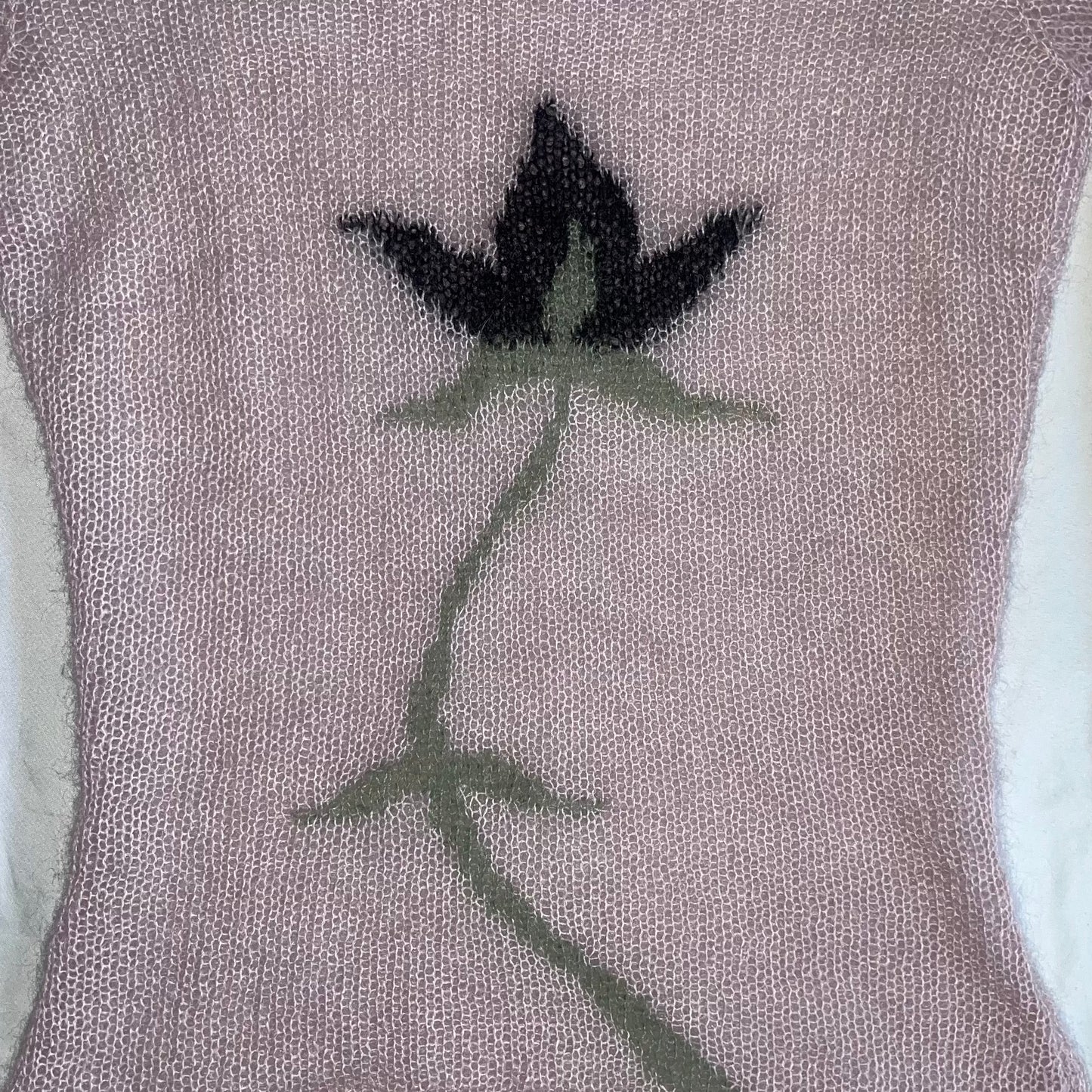 Image is of a sheer light pink mohair long sleeve top with an intarsia flower on the front. The flower is black and green.